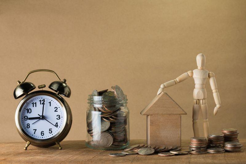 a clock, a jar full of coins, a small wooden house, and a wooden human toy